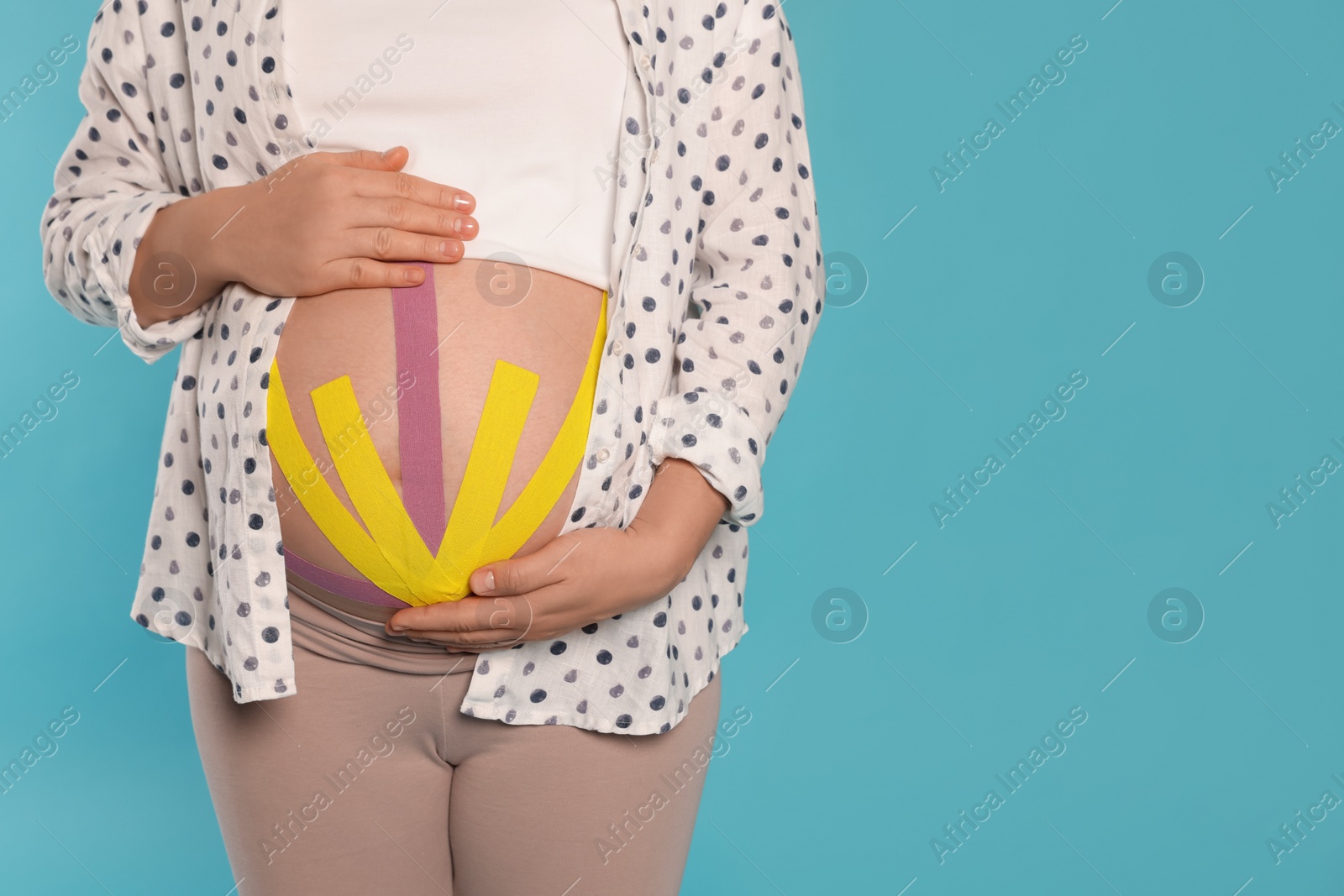 Photo of Pregnant woman with kinesio tapes on her belly against light blue background, closeup. Space for text