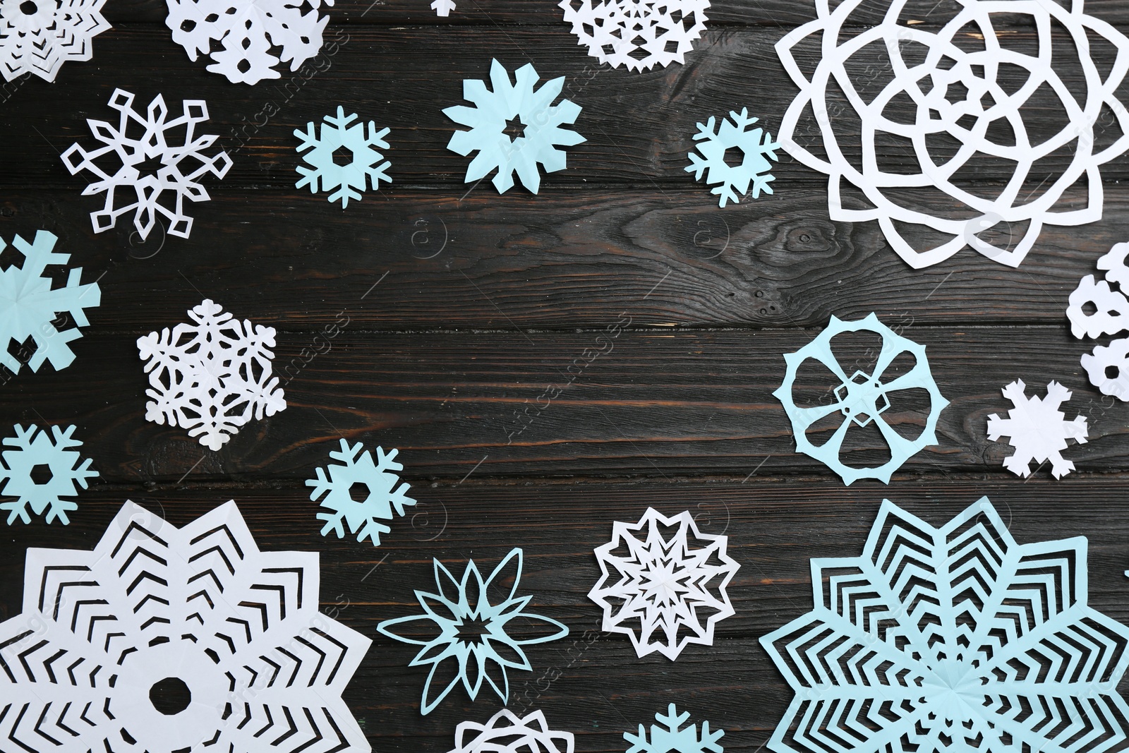 Photo of Frame of paper snowflakes on black wooden table, flat lay. Space for text