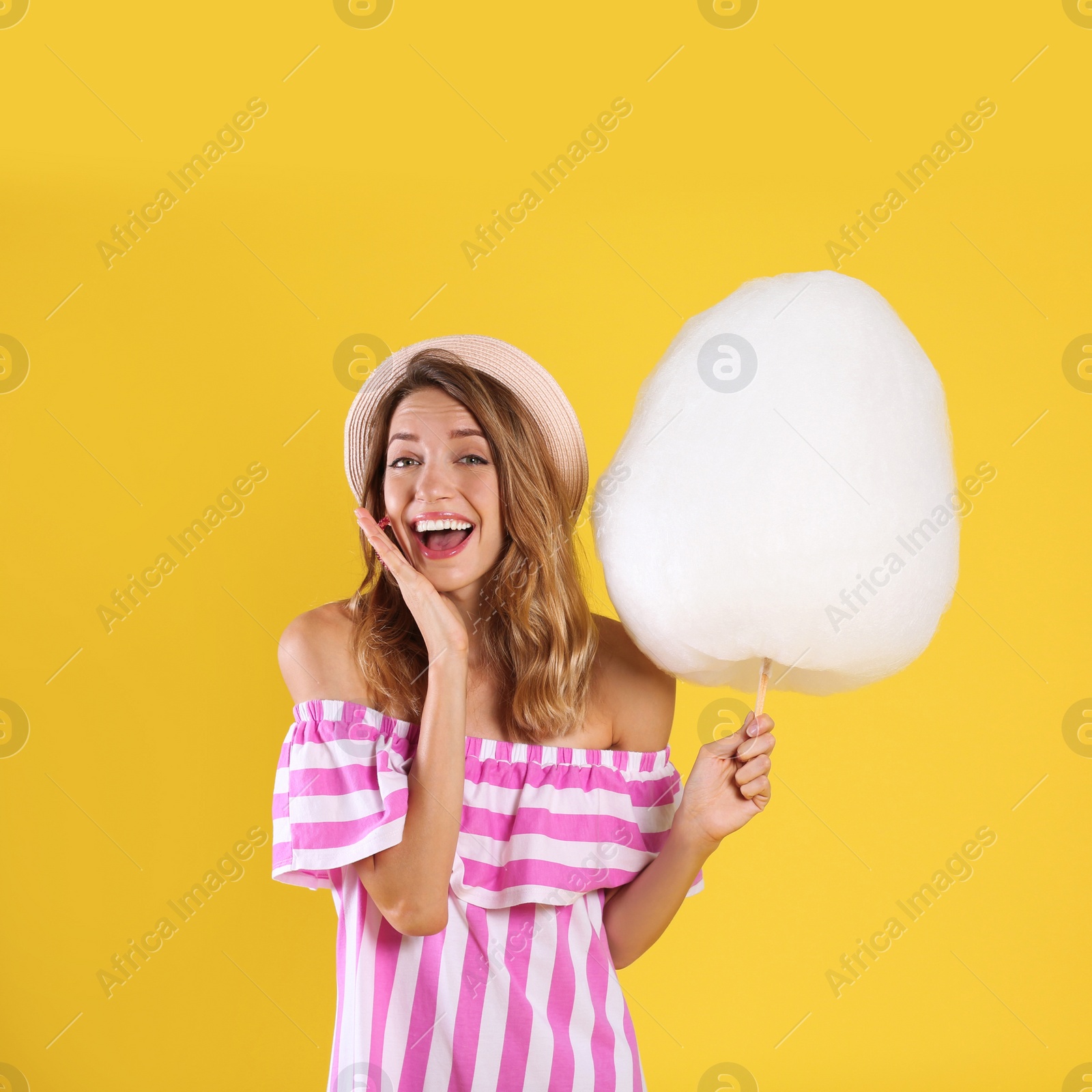 Photo of Emotional young woman with cotton candy on yellow background