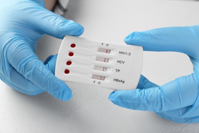 Photo of Doctor holding disposable multi-infection express test at white table, closeup
