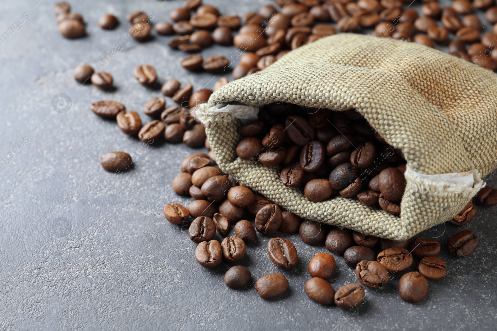 Photo of Bag with roasted coffee beans on grey table, closeup. Space for text