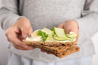 Photo of Woman holding fresh rye crispbreads with quail egg, cream cheese and cucumber slices on light background, closeup
