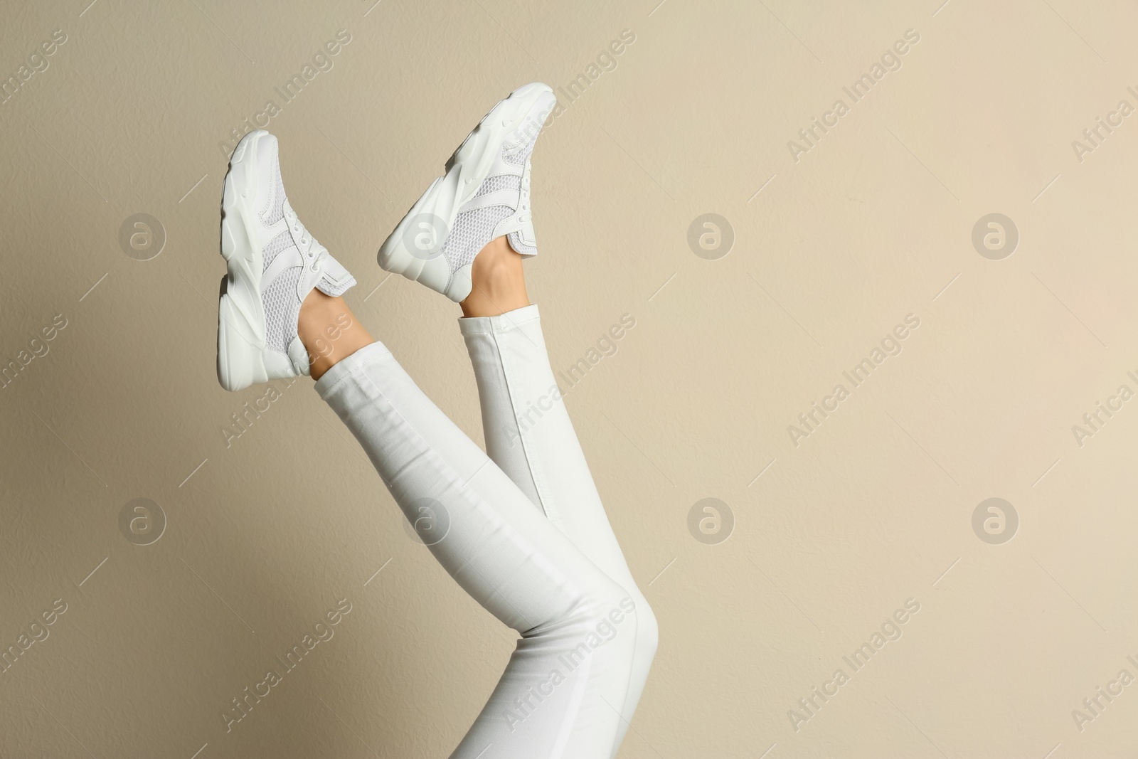 Photo of Woman wearing sneakers on beige background, closeup. Space for text