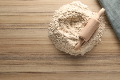 Photo of Pile of flour and rolling pin on wooden table, top view. Space for text