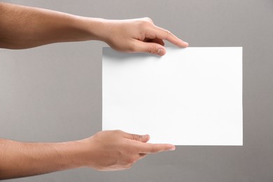 Man holding sheet of paper on grey background, closeup. Mockup for design