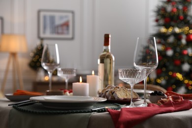 Photo of Christmas table setting with burning candles, appetizers and dishware in room