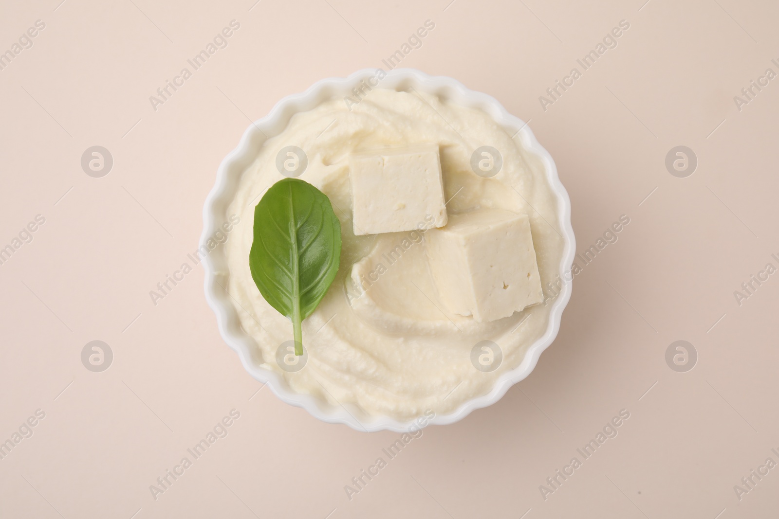 Photo of Delicious tofu sauce and basil leaf in bowl on beige background, top view
