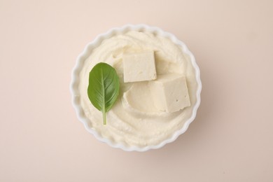 Delicious tofu sauce and basil leaf in bowl on beige background, top view