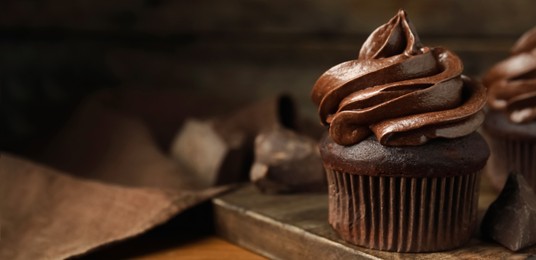 Delicious chocolate cupcake with cream on wooden board, closeup. Space for text