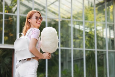 Photo of Smiling woman with cotton candy outdoors. Space for text