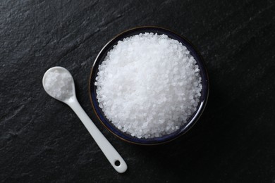 Photo of Organic white salt in bowl and spoon on black table, top view