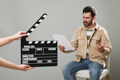 Photo of Emotional actor performing while second assistant camera holding clapperboard on grey background, closeup