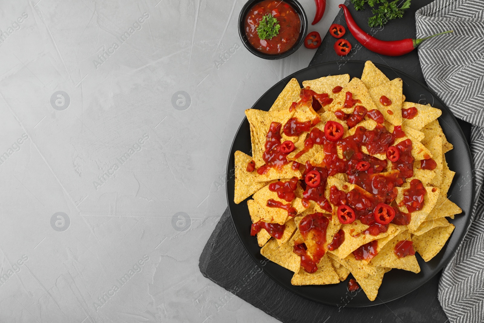 Photo of Plate of Mexican nacho chips with sauce on grey table, flat lay. Space for text