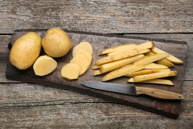 Photo of Whole and cut potatoes with knife on wooden table, top view. Cooking delicious french fries