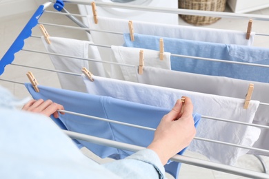Woman hanging clean laundry on drying rack indoors, closeup