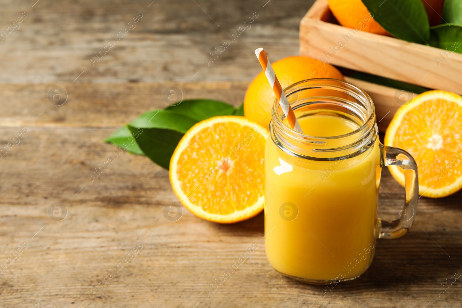 Photo of Mason jar of orange juice and fresh fruits on wooden table. Space for text