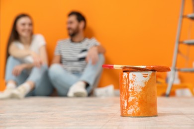 Photo of Designers sitting near freshly painted orange wall indoors, focus on can of paint