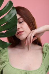 Portrait of beautiful woman with freckles and monstera leaf on pink background