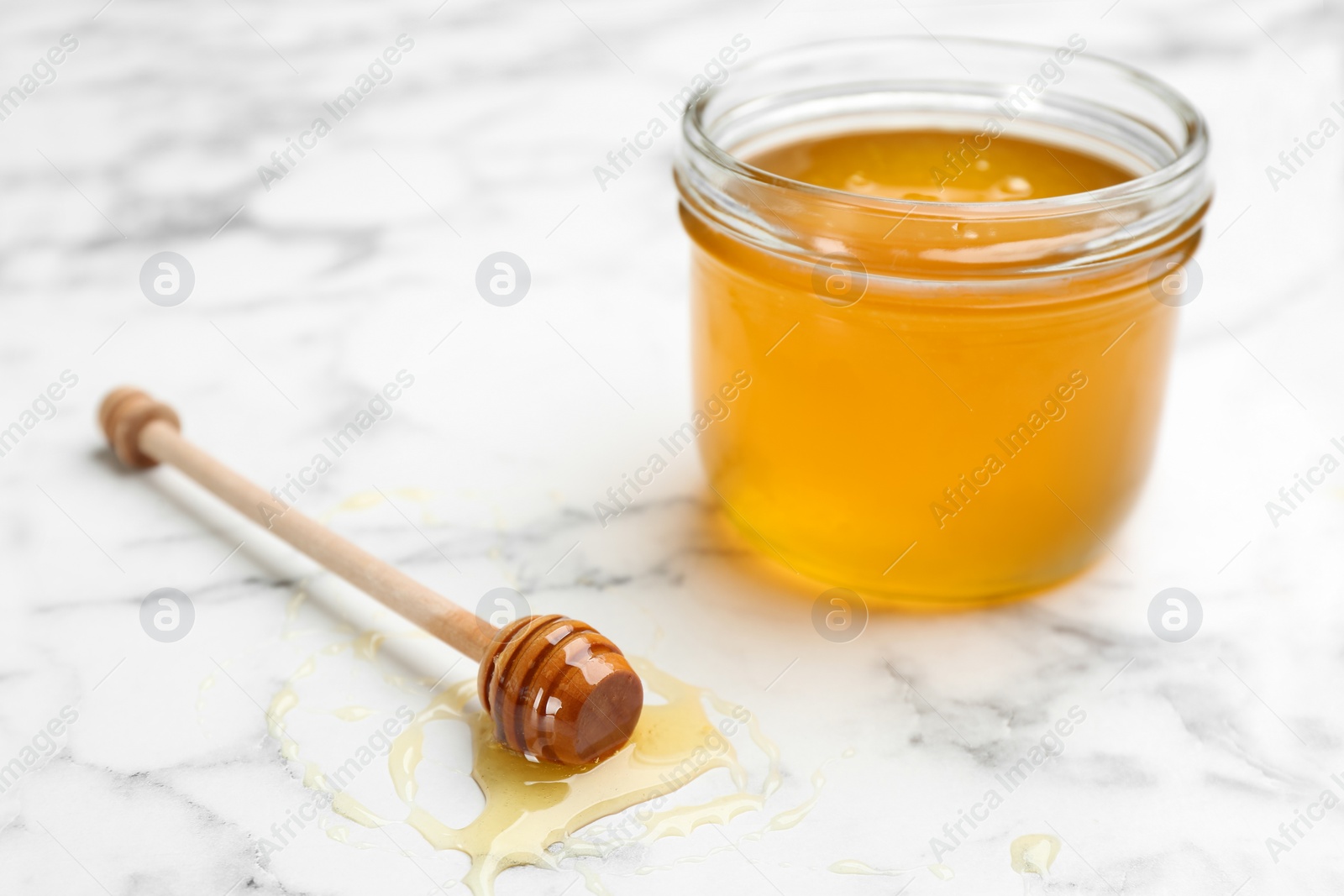 Photo of Tasty honey on white marble table, closeup