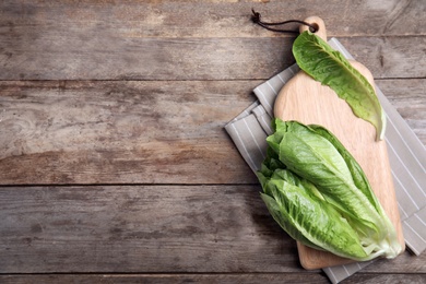 Photo of Board with fresh ripe cos lettuce on wooden background, top view