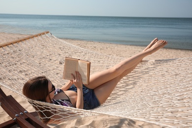 Photo of Young woman reading book in hammock on beach