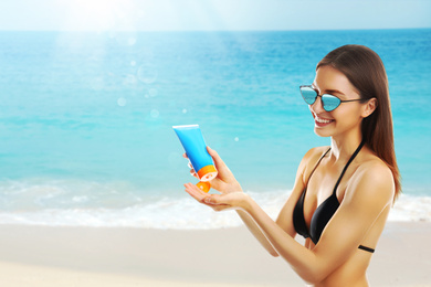 Young woman applying sun protection cream at beach, space for text