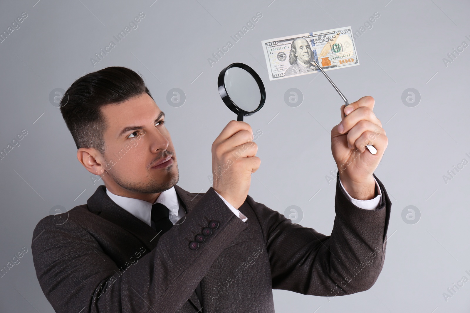 Photo of Expert authenticating 100 dollar banknote with magnifying glass on light grey background. Fake money concept
