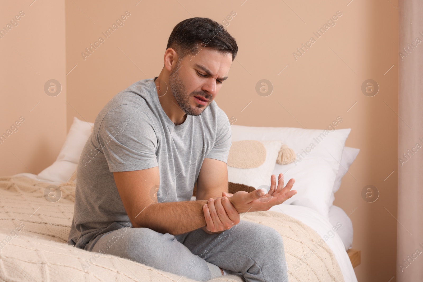 Photo of Man suffering from pain in his hand on bed indoors
