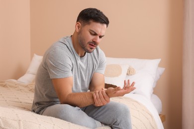 Man suffering from pain in his hand on bed indoors