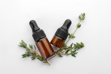 Photo of Bottles with thyme essential oil and fresh herb on white background