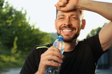 Photo of Happy man with bottle of water outdoors on hot summer day. Refreshing drink