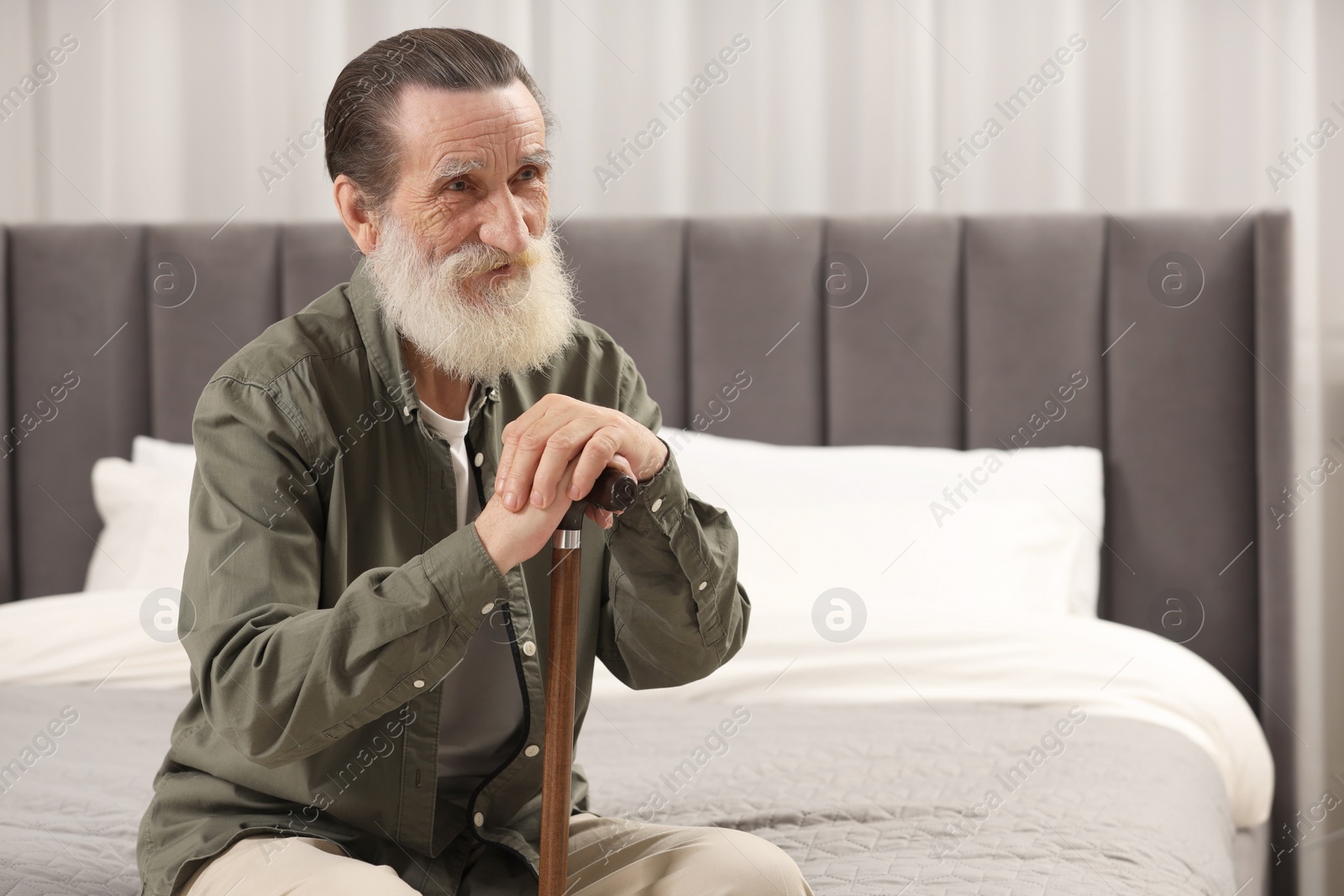 Photo of Senior man with walking cane on bed at home