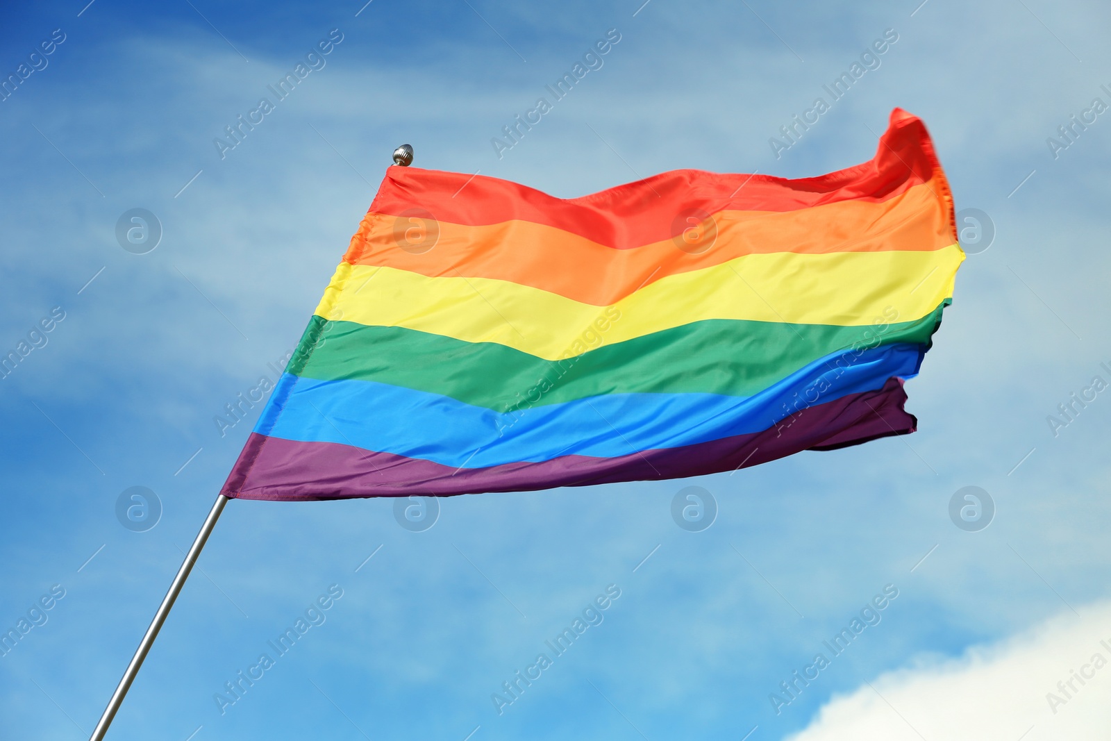 Photo of Bright rainbow gay flag fluttering against blue sky. LGBT community