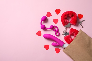 Photo of Paper shopping bag with different sex toys on pink background, flat lay. Space for text