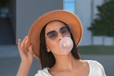 Photo of Beautiful woman in stylish sunglasses blowing gum outdoors on sunny day