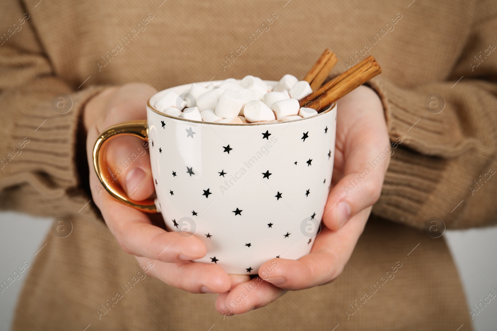Photo of Woman holding cup of delicious hot chocolate with marshmallows and cinnamon sticks, closeup