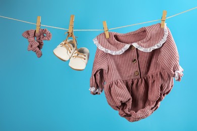 Photo of Baby clothes and accessories hanging on washing line against light blue background