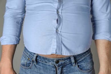 Overweight man in tight shirt on grey background, closeup