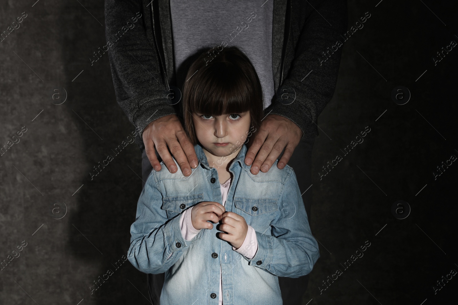 Photo of Scared little girl and adult man on dark background. Child in danger