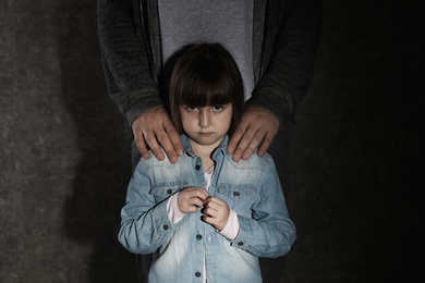 Scared little girl and adult man on dark background. Child in danger