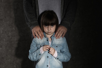 Photo of Scared little girl and adult man on dark background. Child in danger