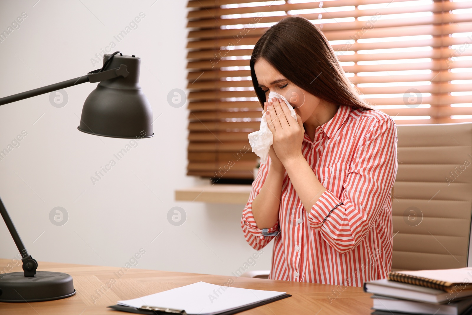 Photo of Sick young woman sneezing at workplace. Influenza virus