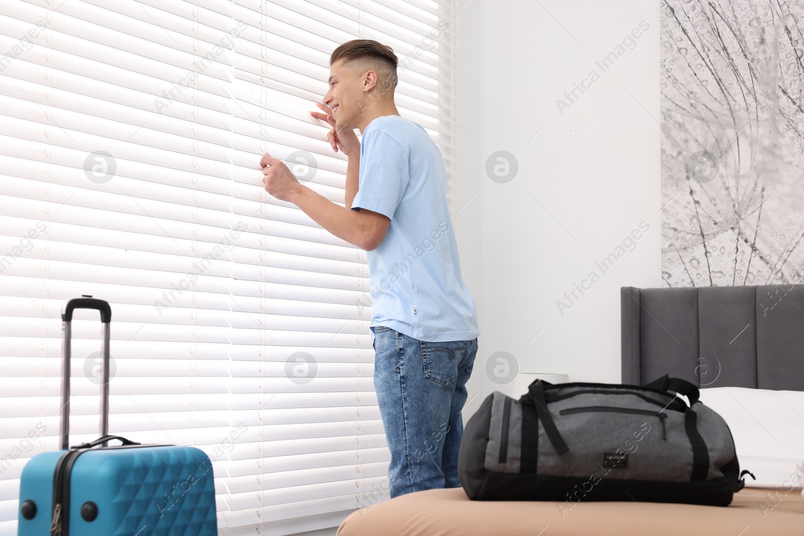 Photo of Smiling guest looking through blinds in stylish hotel room