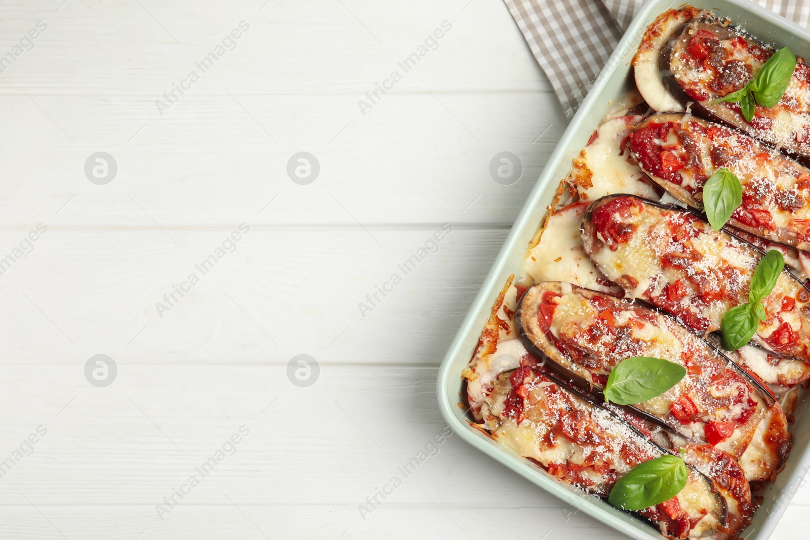 Photo of Baked eggplant with tomatoes, cheese and basil in dishware on white wooden table, top view. Space for text