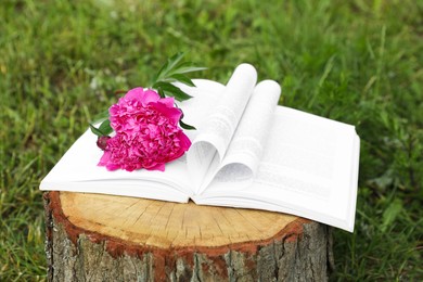 Photo of Open book with beautiful peony on tree stump outdoors