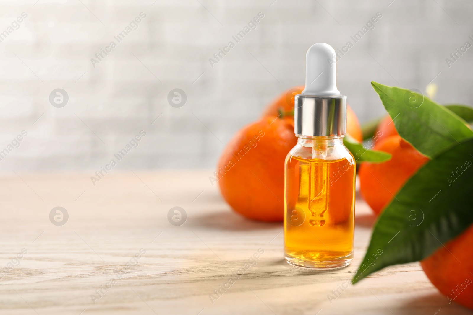 Photo of Bottle of tangerine essential oil and fresh fruits on white wooden table, closeup. Space for text