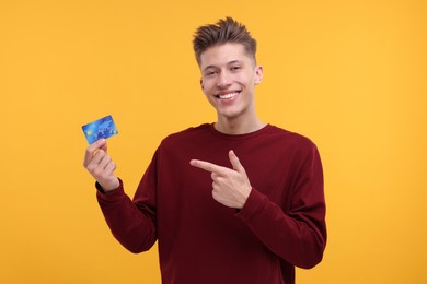 Photo of Happy man pointing at credit card on yellow background