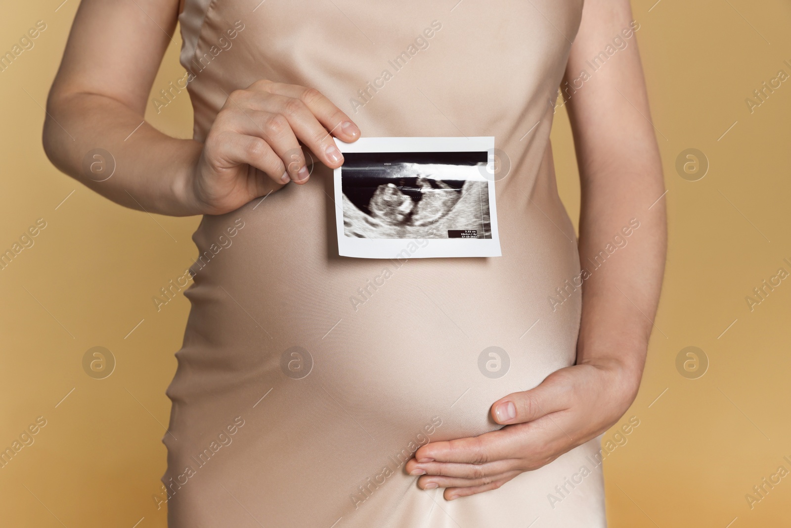 Photo of Pregnant woman with ultrasound picture of baby on beige background, closeup