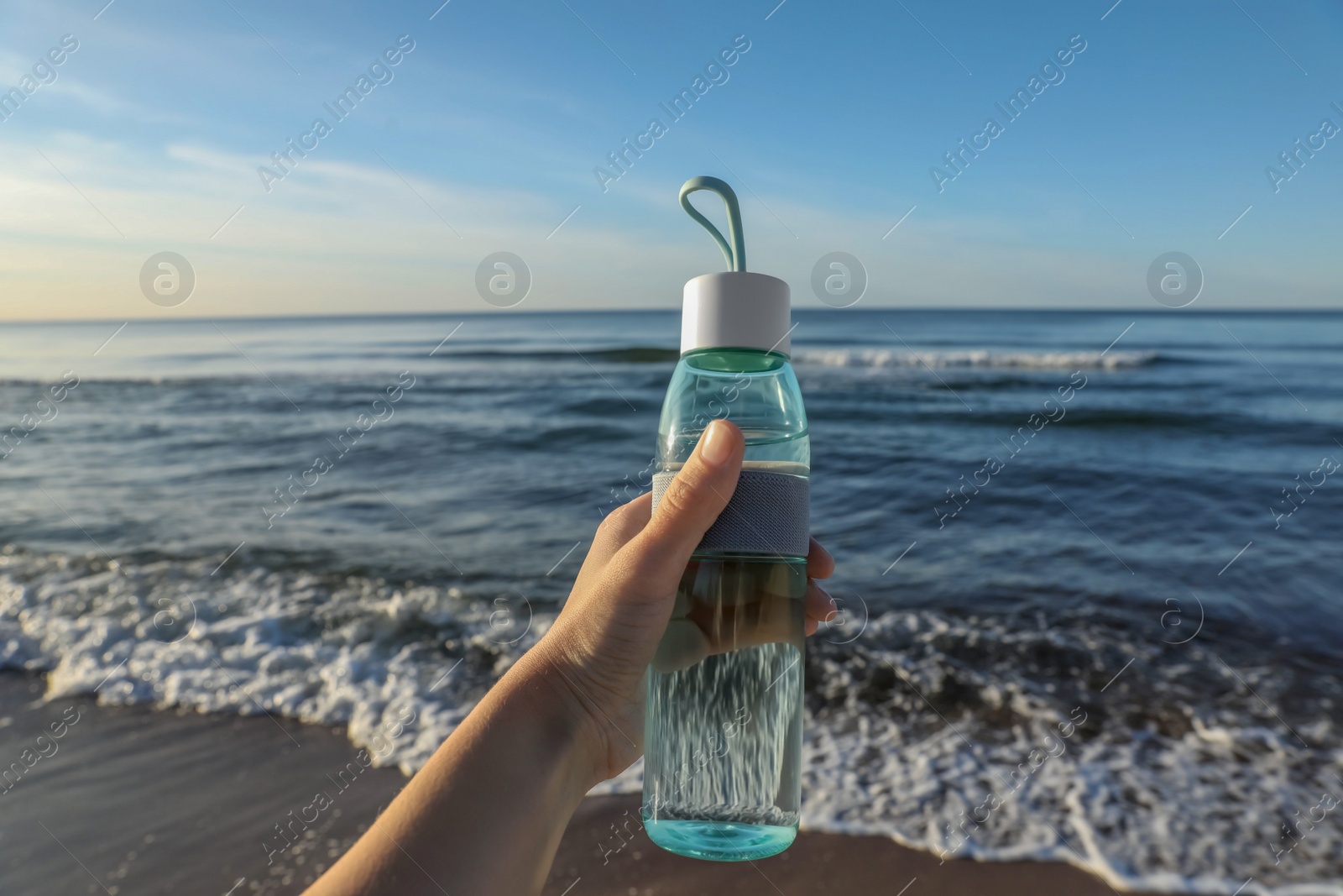 Photo of Woman holding glass bottle with water near sea, closeup