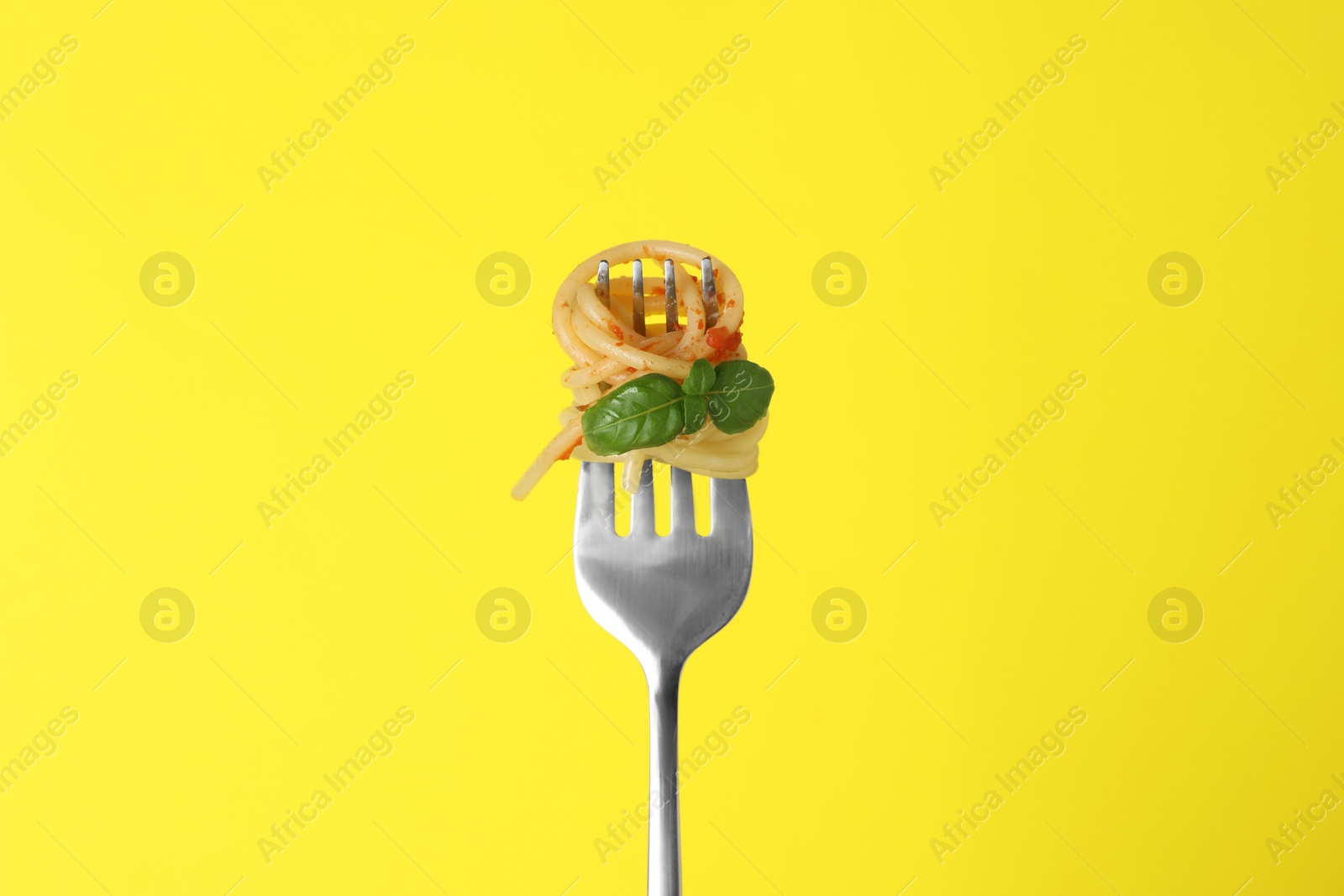 Photo of Fork with tasty pasta, basil and tomato sauce on yellow background